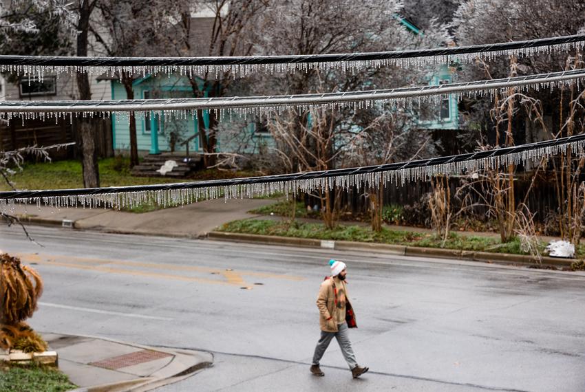 A man walks underneath icy power lines after a winter storm in north Austin on Feb. 1, 2023.
