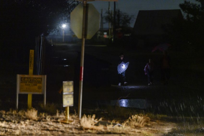 Margarita Soto, far right, walks to their community school-bus stop in the rain with her grandchildren Cameron and Lin Soto before dawn Tuesday, Sept. 12, 2023 in West Odessa.
