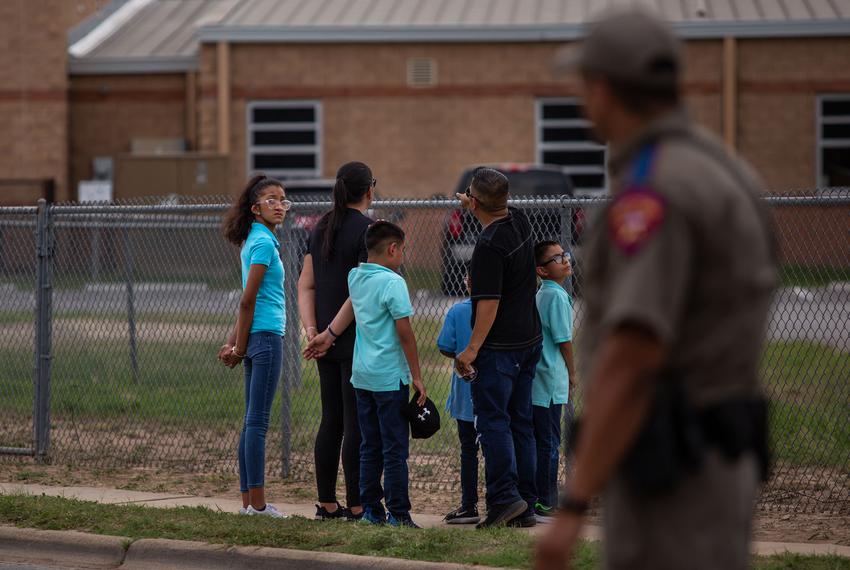A family looks over a chain-link fence towards the back door of Robb Elementary School in Uvalde on May 30, 2022. The 18-year-old gunman entered through this door and opened fire on a classroom, killing 19 students and two teachers.