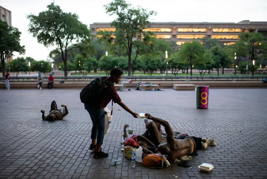 Michelle Smith, Outreach and Engagement Manager at The Bridge, hands a health kit to a homeless man sleeping outside of the Dallas Public Library in Dallas, Texas on Thursday, July 21, 2022. (Emil Lippe for The Texas Tribune)
