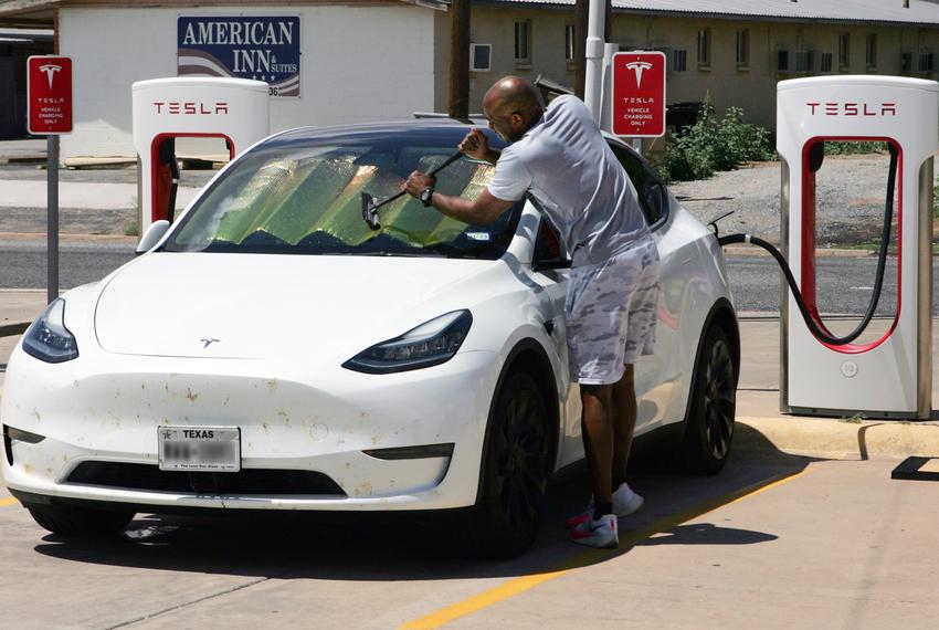 While waiting for the battery in his Tesla EV to charge, a traveler cleans the windshield on his vehicle at a service station in Childress on Aug. 23, 2022.